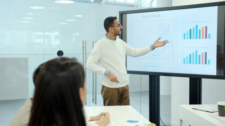 A man presents prodcut launch and sales data from a projection screen to his colleagues in the office.